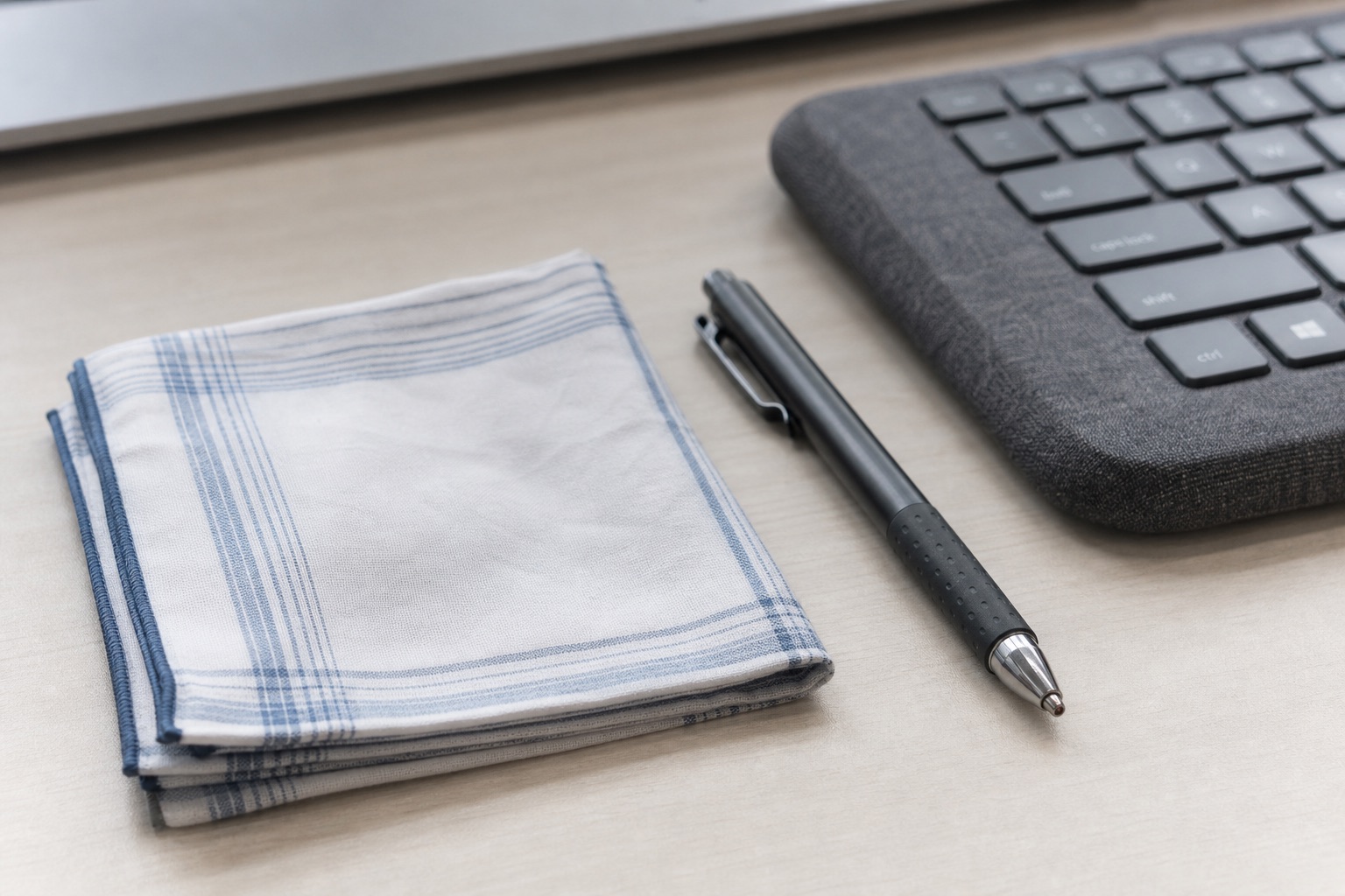 Stilleven op een licht bureau: een opgevouwen katoenen zakdoek, een pen met rubberen greep en een toetsenbord met textiele bekleding